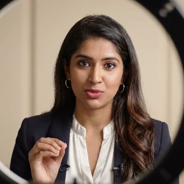 A presenter with a lapel microphone talking to camera, lit by a ring light